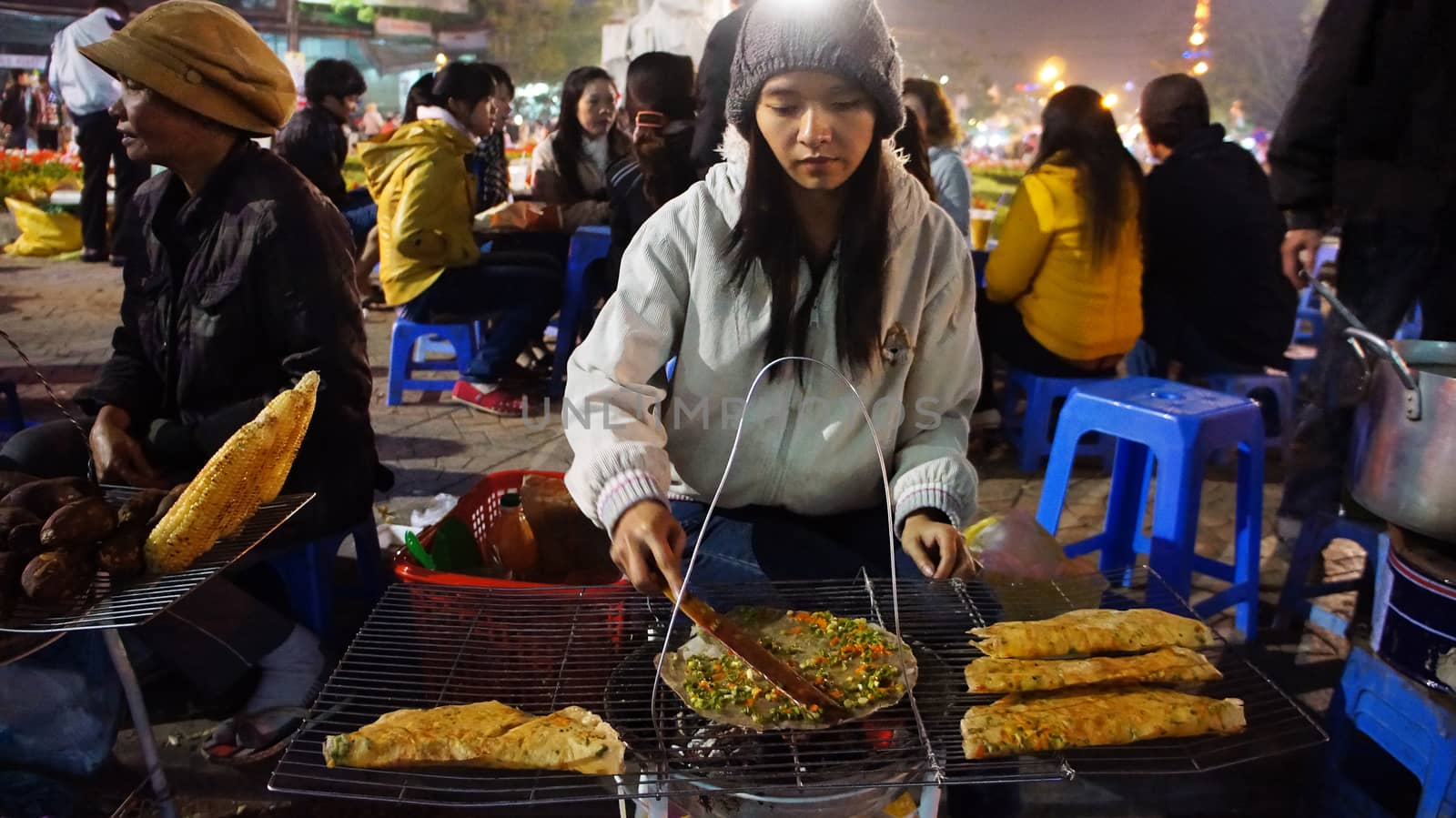 DA LAT, VIET NAM- DEC 29: Vietnamese street food vendor grill baked girdle cake- one of eating street, people at oudoor market in cold night- lifestyle of young person in Dalat, Vietnam on Dec 29,2013