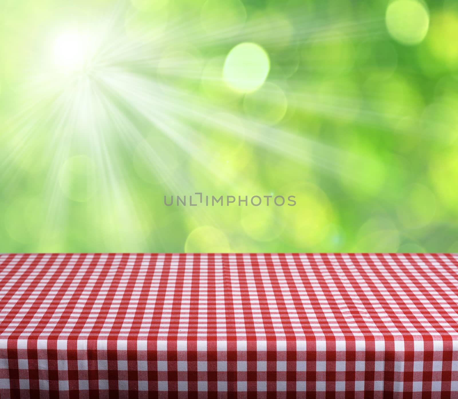 Empty table with red gingham tablecloth over green bokeh background. Great for product display montages