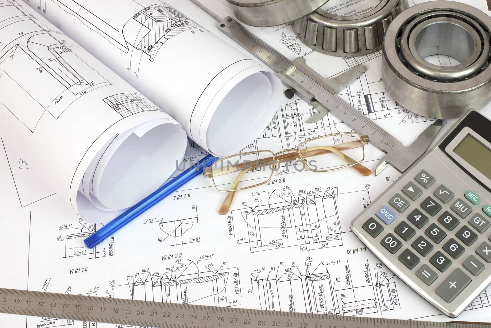 Construction drawings, caliper, bearing, calculator, pen, ruler and glasses. Desk Engineer