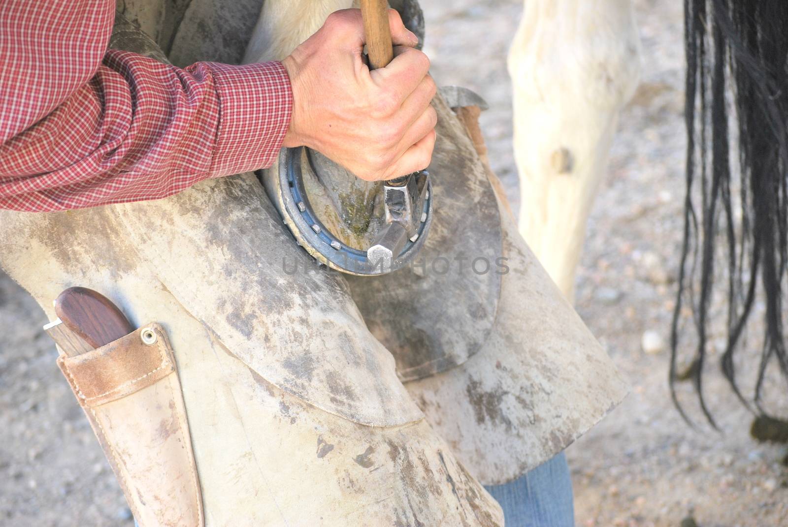 Male farrier working on a horseshoe outside.