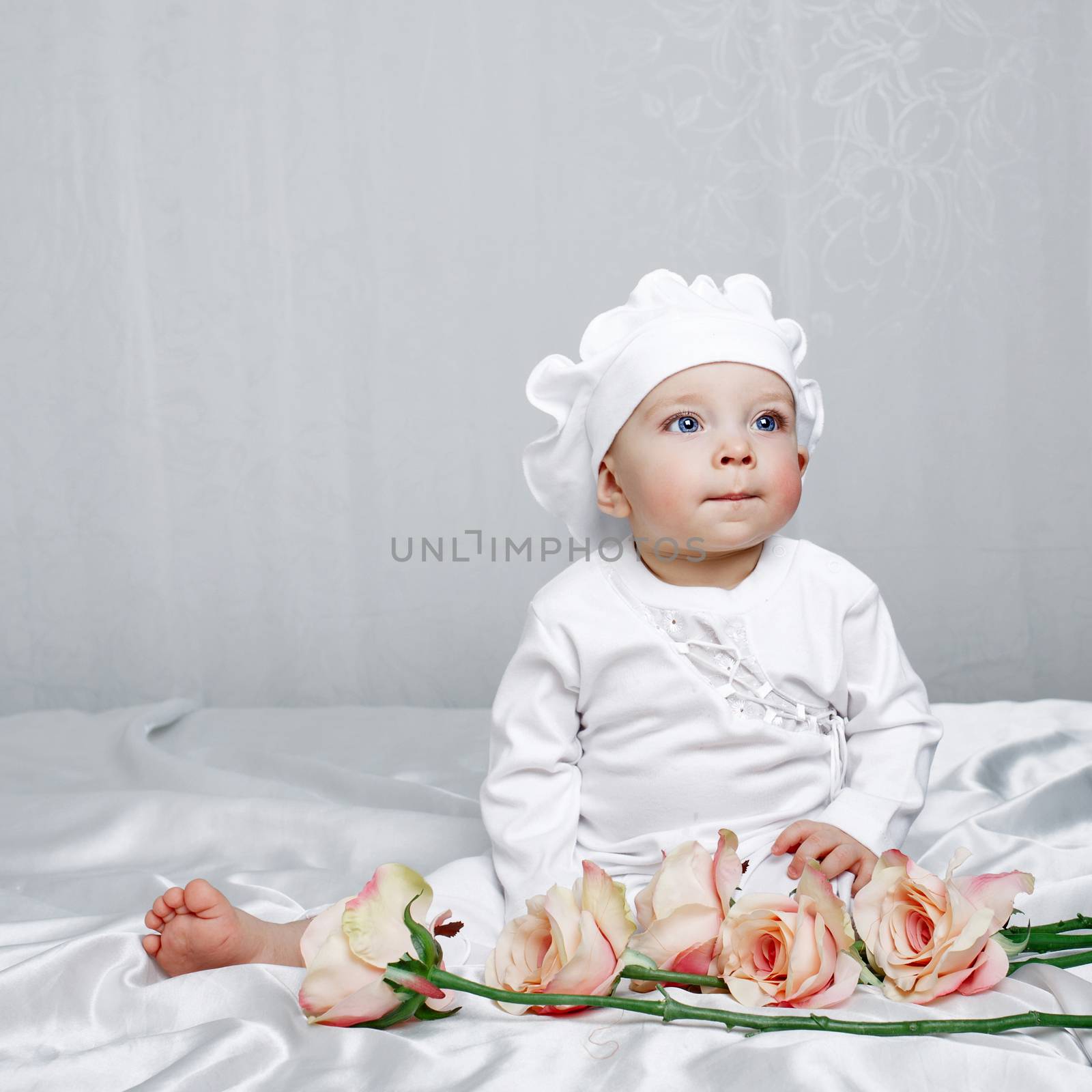 Little girl sitting on silk sheets lie at the feet of flowers