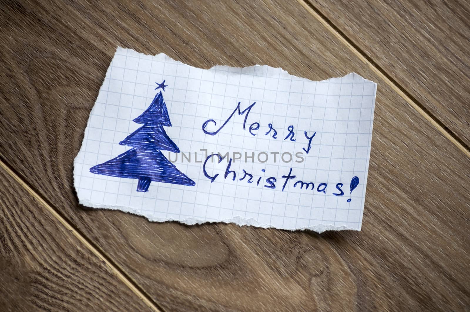 Merry Christmas written on piece of paper, on a wood background.