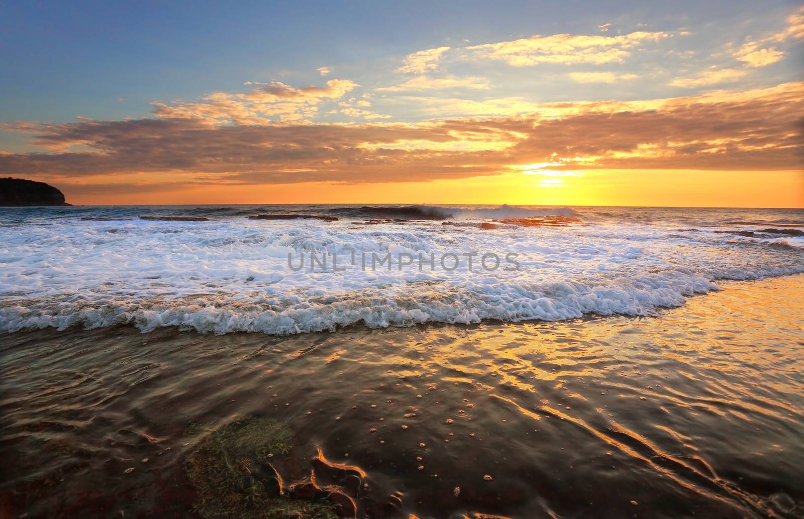 Waves crash and the water flows onto the rock shelf during high tide at sunrise.