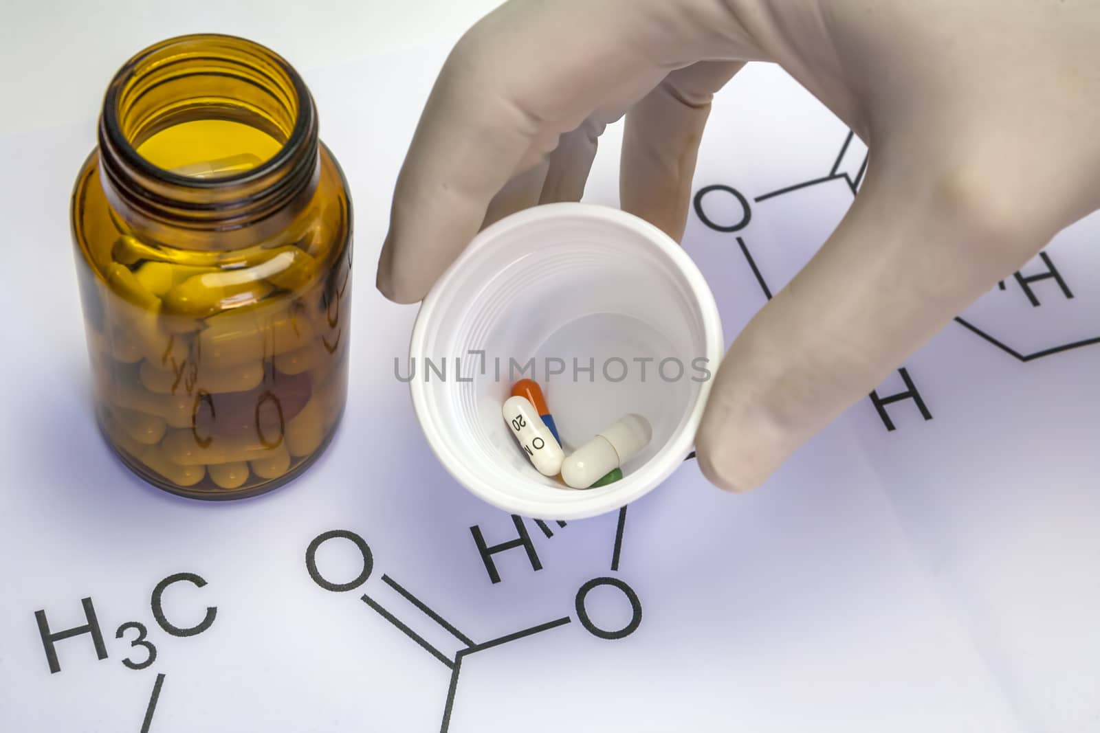 Chemistry science formula and tablets, Hand with white latex glove holds a plastic cup with several pills