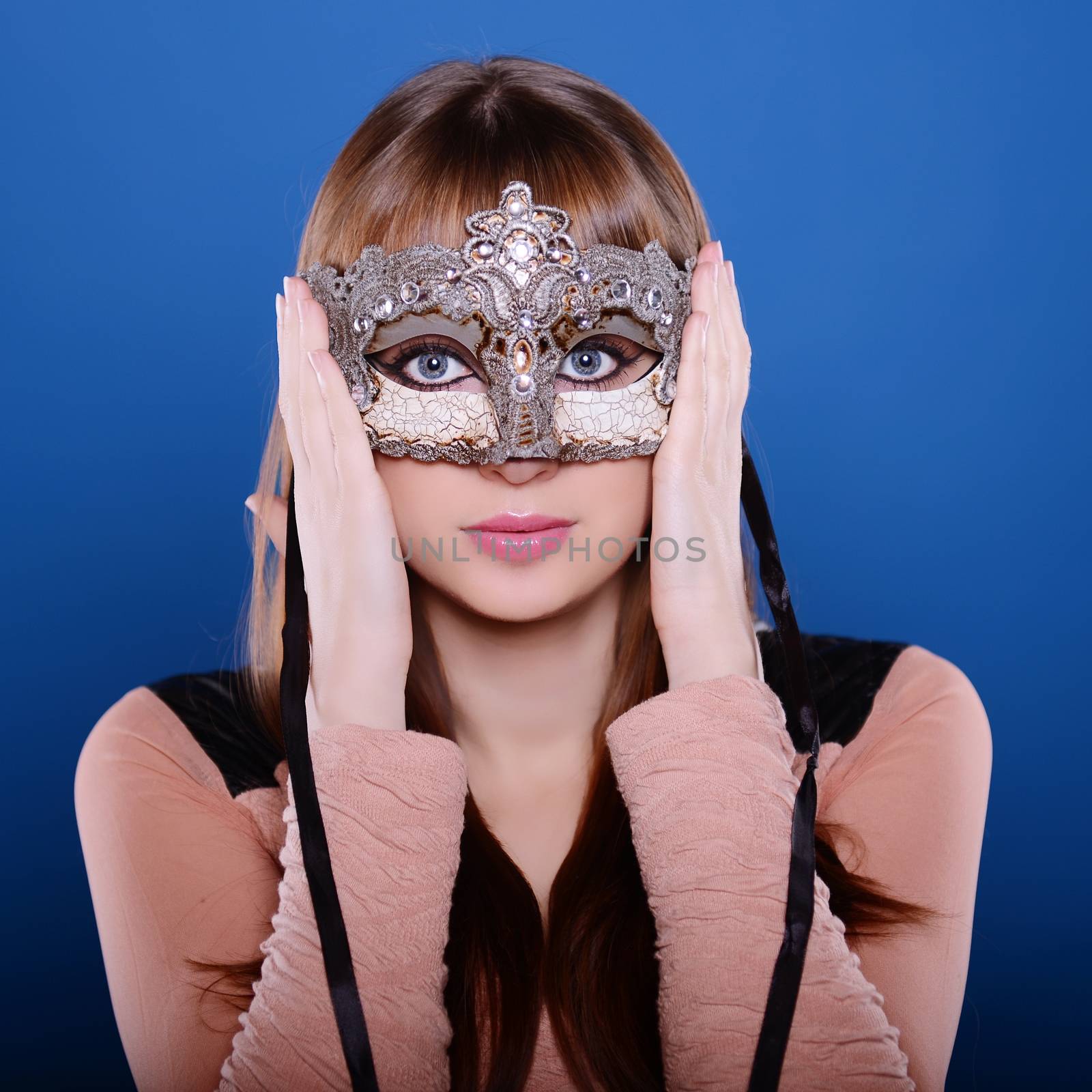 Beautiful caucasian brunette in carnival mask over blue background