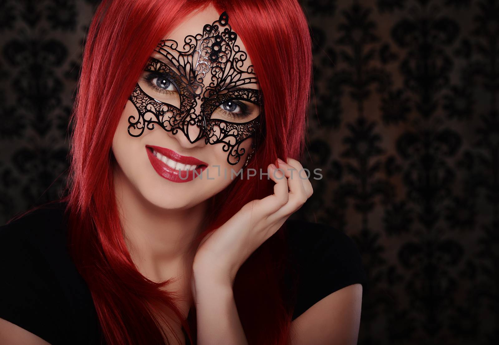 Beautiful caucasian red haired woman in carnival mask over blue background
