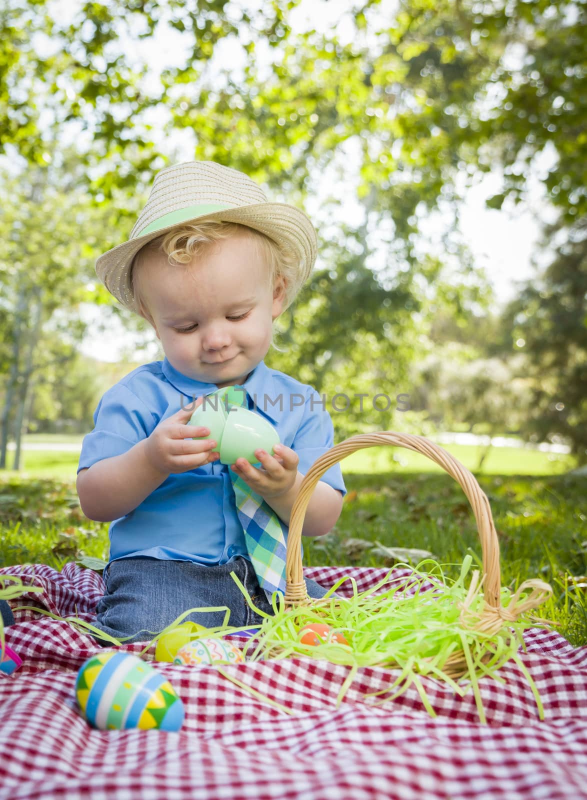 Cute Little Boy Wearing Hat Enjoying His Easter Eggs on Picnic Blanket Outside in the Park.