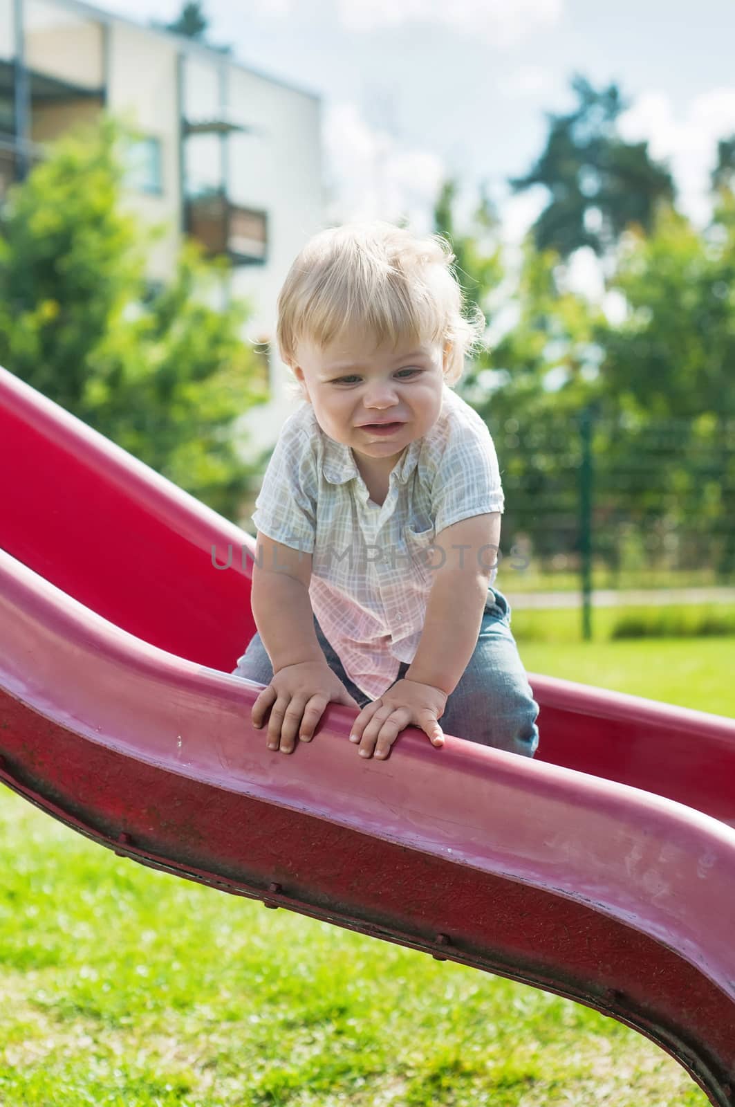 Baby boy on a red slide in playground