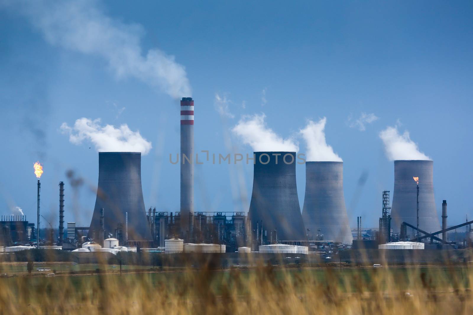 Energy production plant with cooling towers, chimneys and gas flame