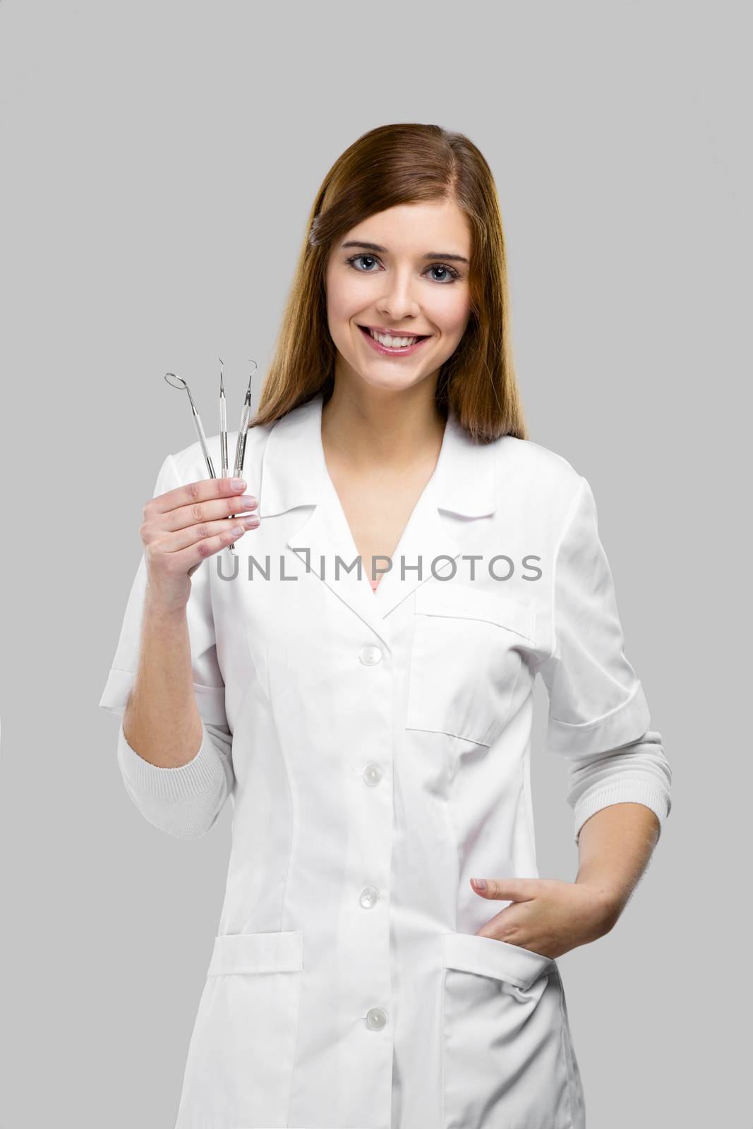 Beautiful and attractive female dentist with tools, over a gray background