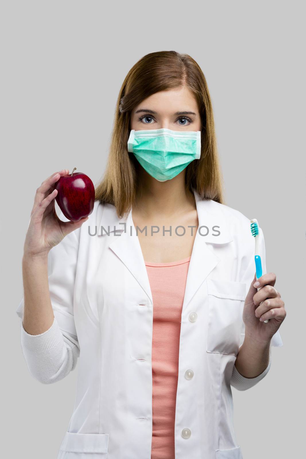 Beautiful and attractive female dentist holding tools and a red apple, isolated over a white background