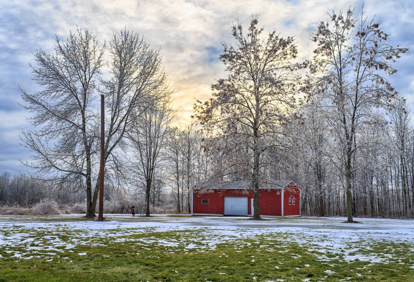Winter scene of ice covered trees and barn. The sky is cloudy at sunset. 