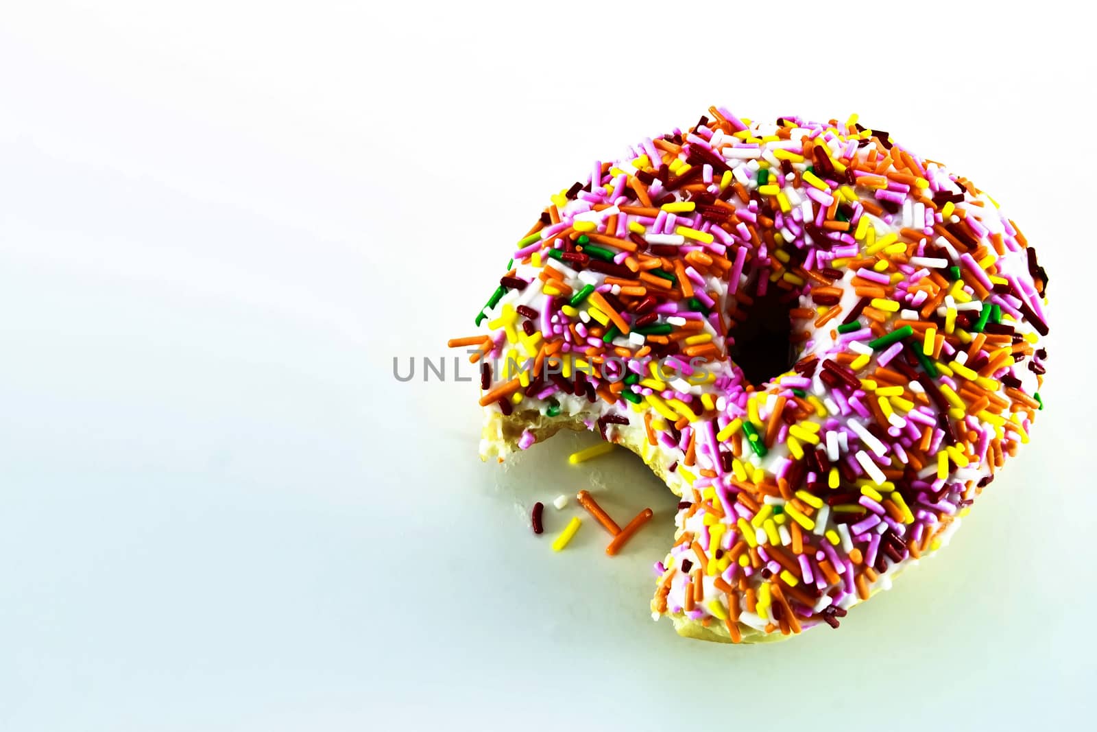 Delicious donut covered with rainbow sprinkles. Someone took a bite of this colorful pastry.