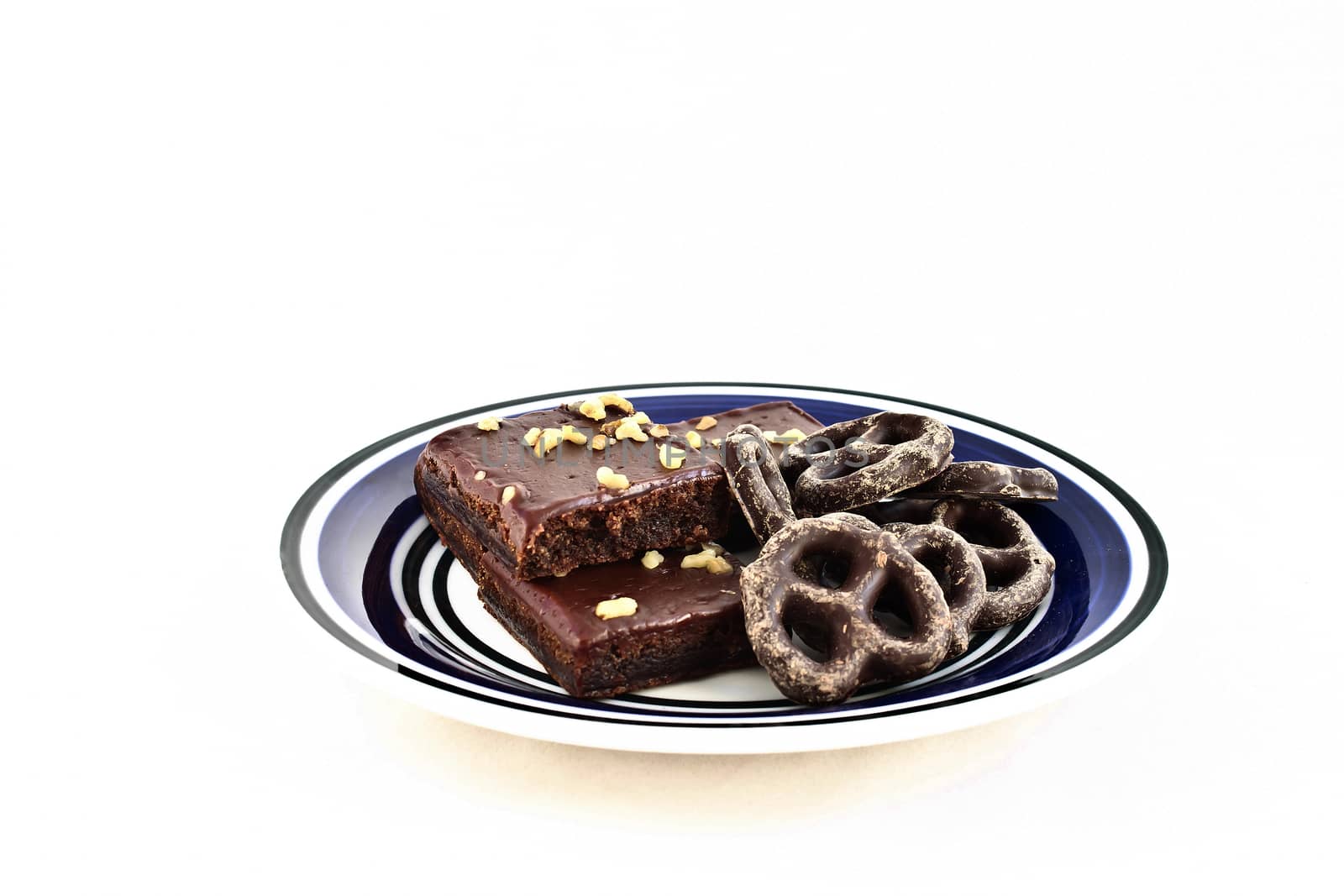 Chocolate covered pretzels and walnut-covered fudge brownie squares on a white and blue plate.