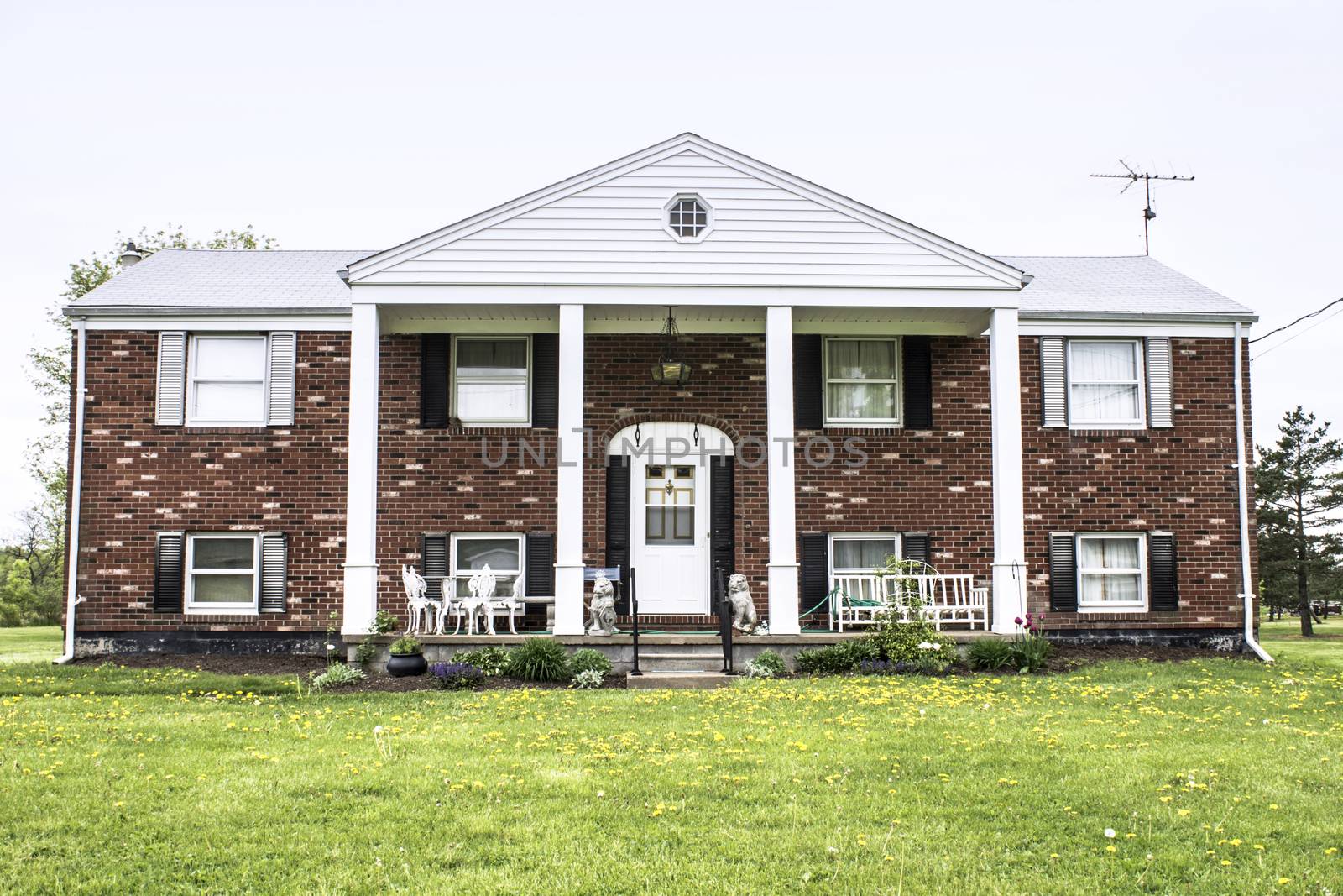 Big brick raised ranch style home with white pillars and fresh landscaping. This American structure was built in the 1970s.