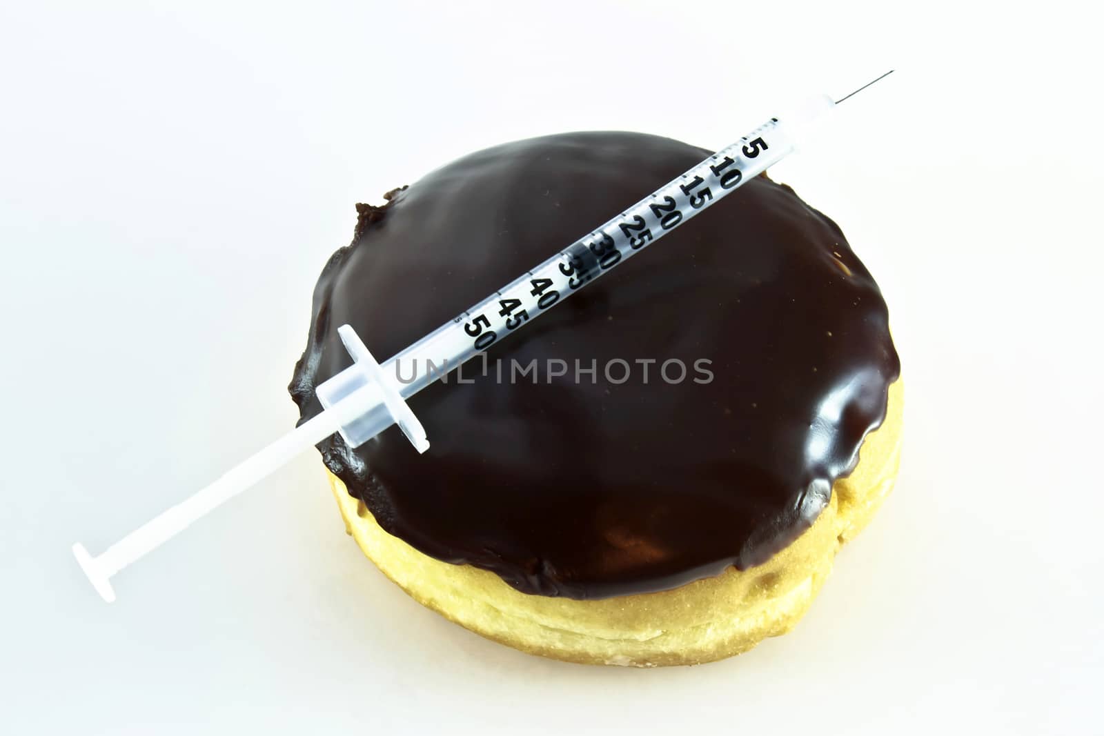 Sugary chocolate frosted donut with a diabetic insulin needle lying across. Concept piece. 