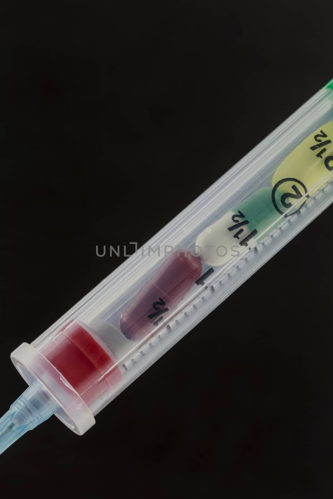 Intravenous syringe filled with a dosage of colorful pills on black.