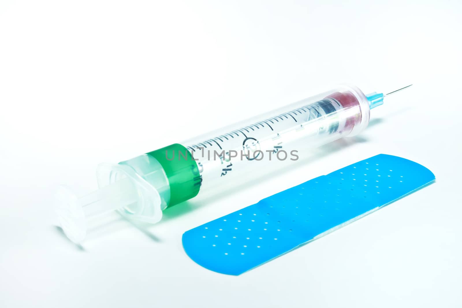 Empty syringe and needle next to a blue adhesive bandage.