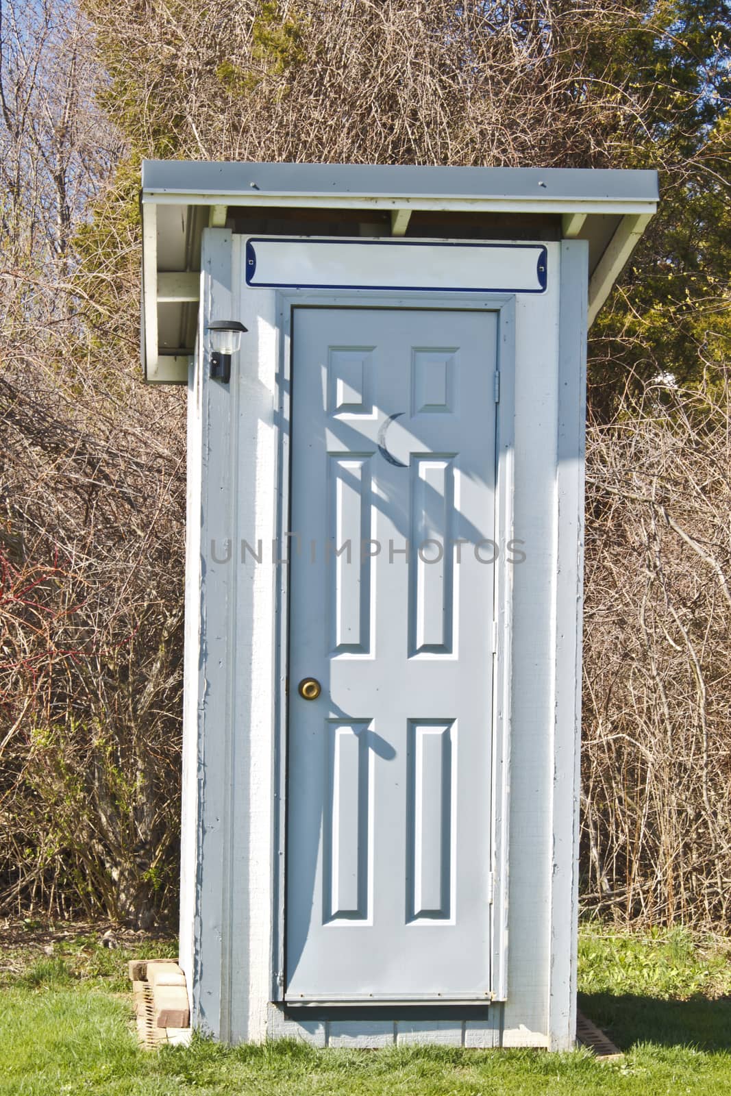 Newly constructed outhouse with gray door and white paneling. 