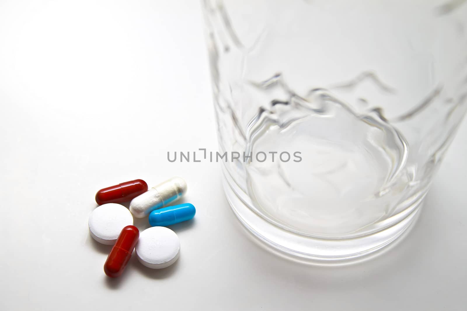 Pile of red, blue, and white pills of varying sizes with water glass. All on white background.