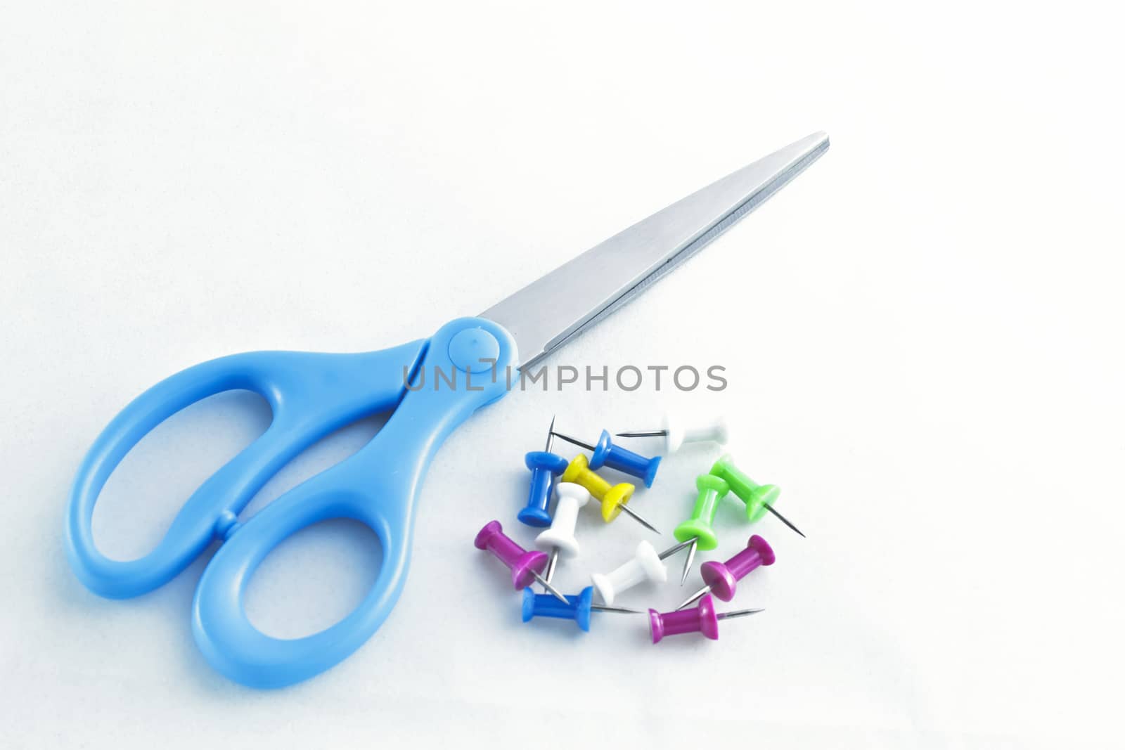 Blue handle scissors lay next to a pile of colorful tacks.