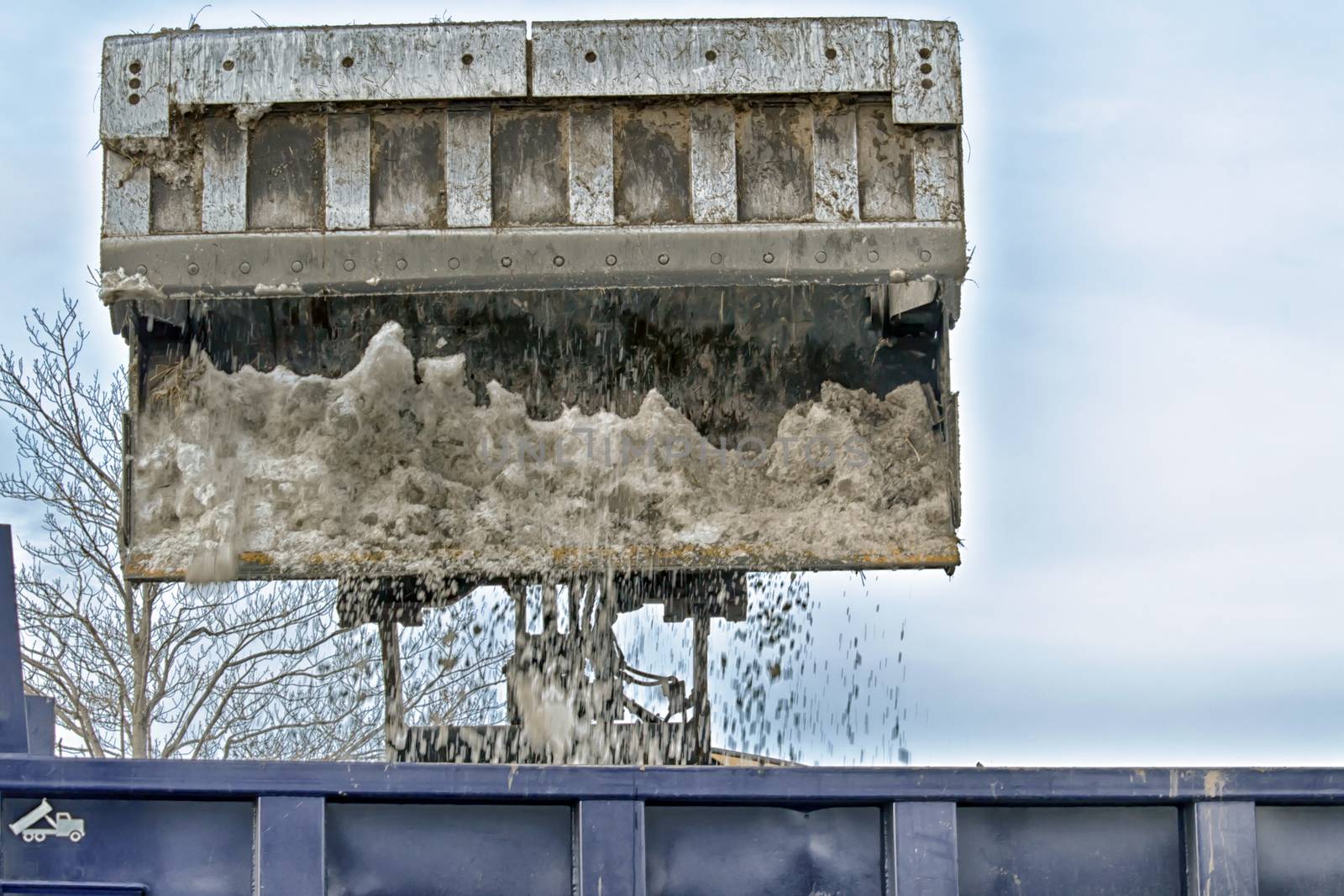Bulldozer bucket drops snow into blue city dumptruck.