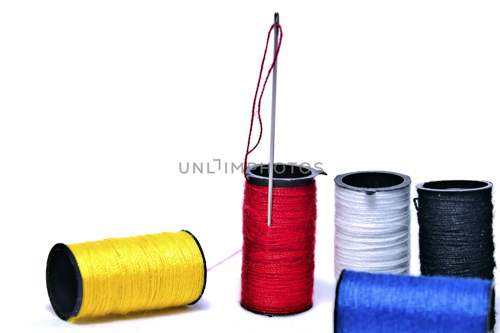 Five spools of thread in a variety of colors. A needle is sticking out from one. 