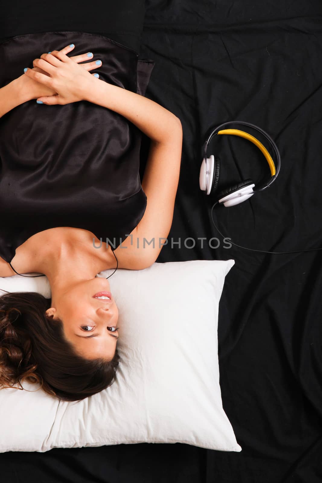 A young girl laying in bed, smiling with headsets
