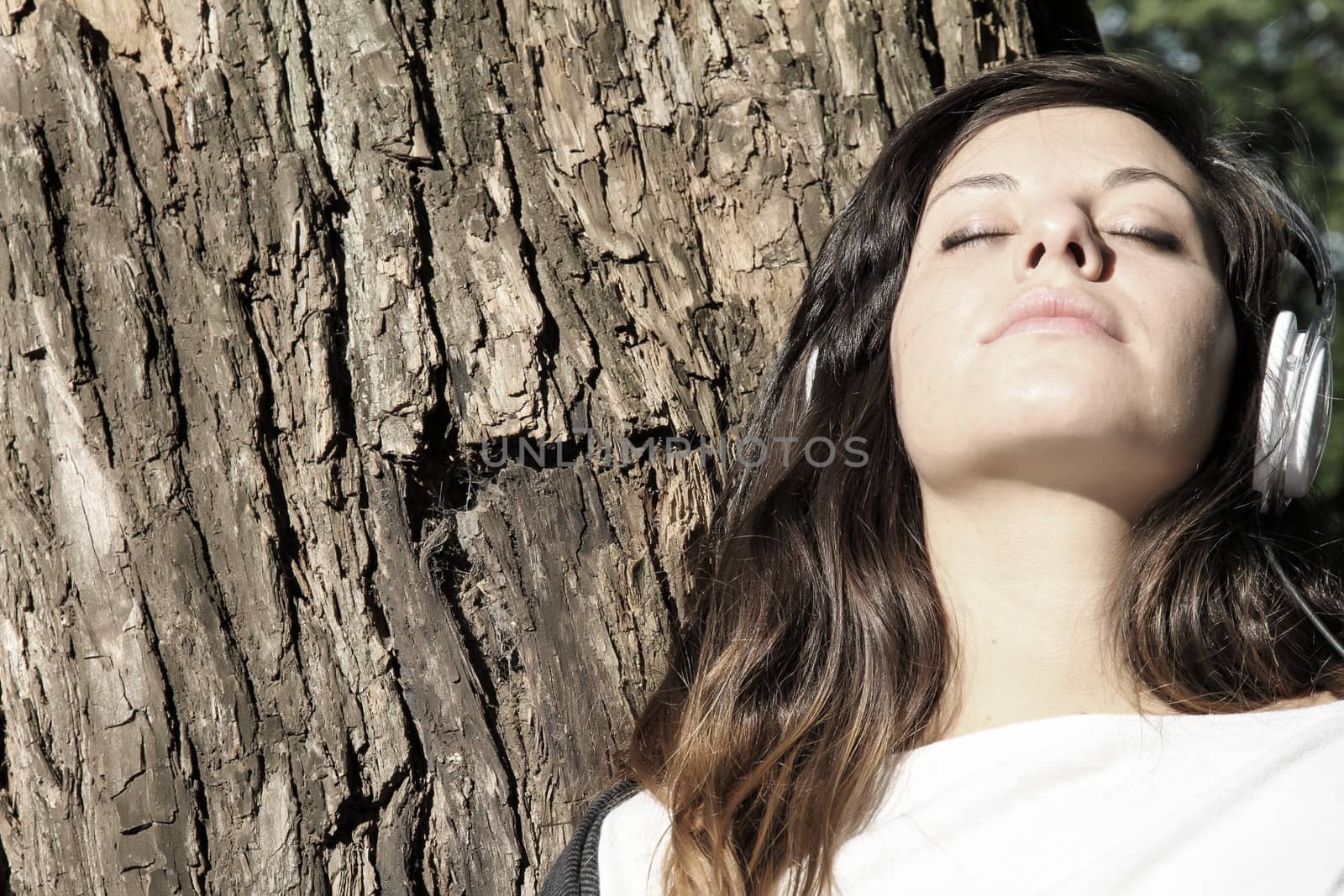 A young woman enjoying Music and sitting on a branch.
