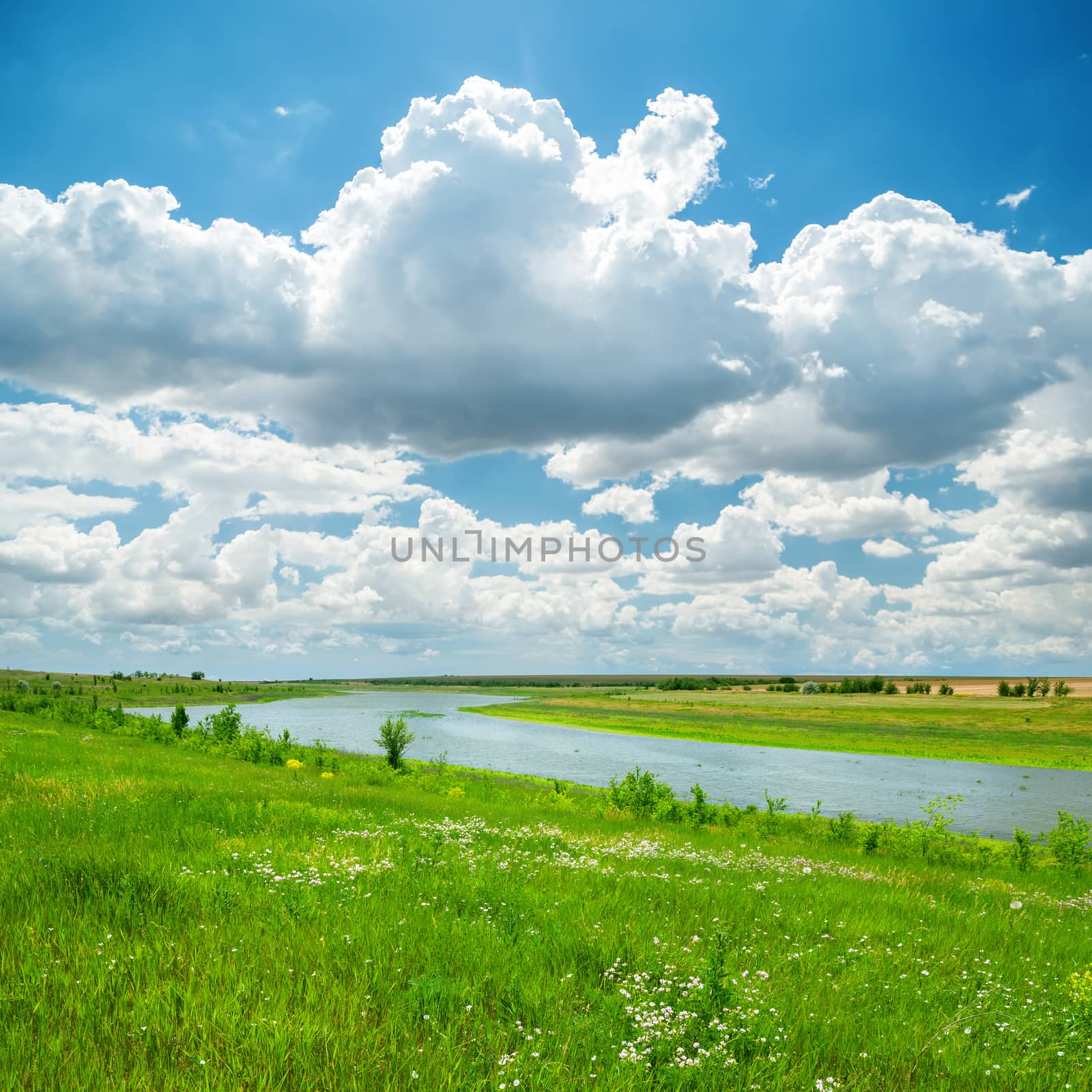 river in green landscape and low clouds in blue sky