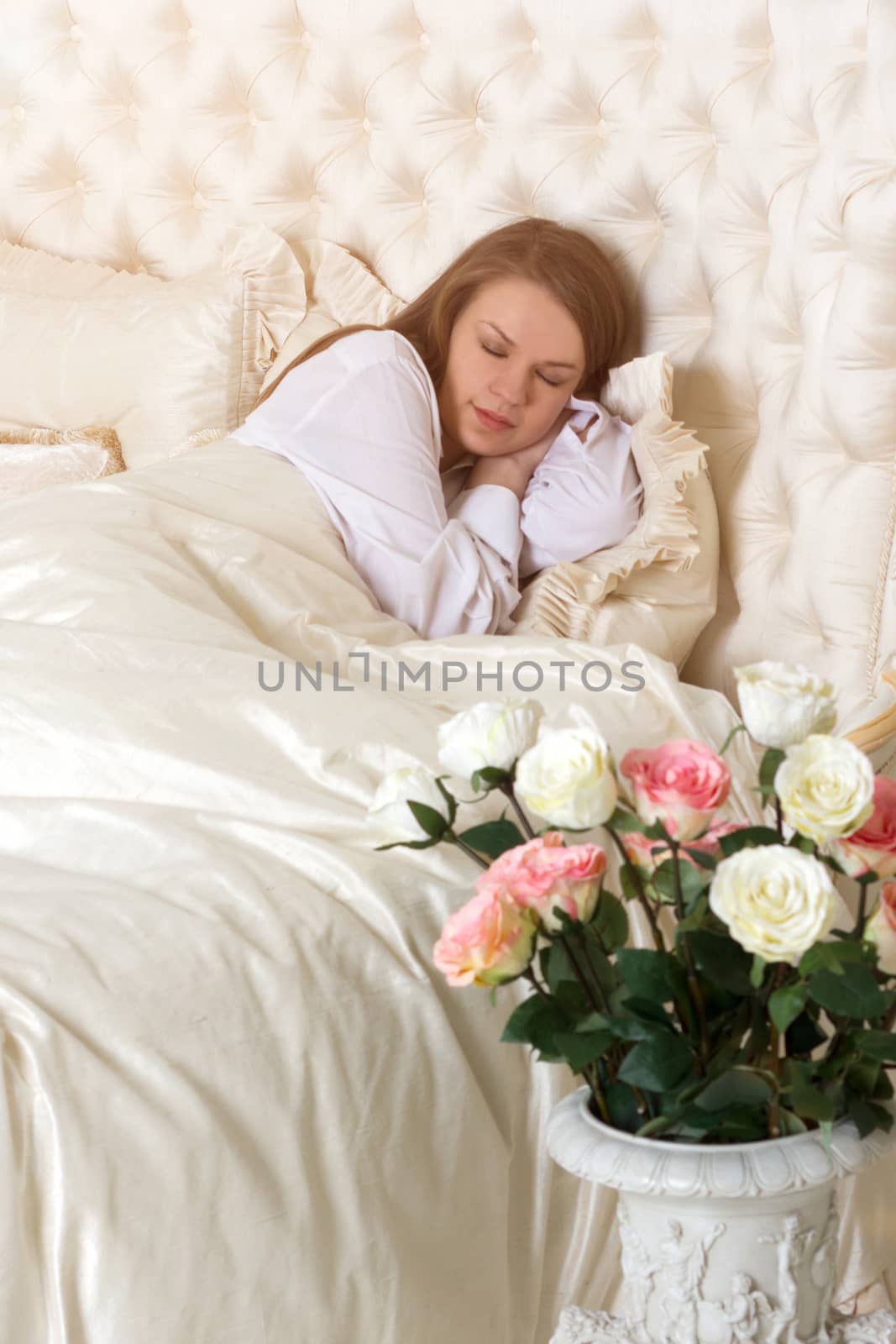 Romance. Beautiful sleeping woman in white bed with red roses