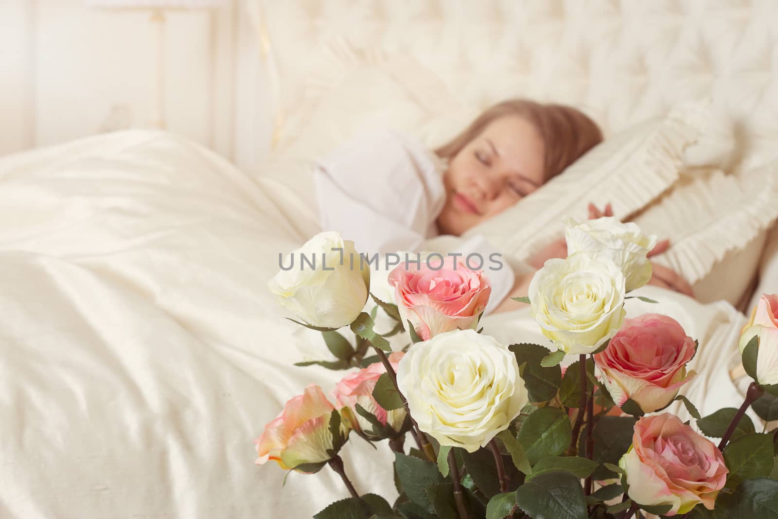 Romance. Beautiful sleeping woman in white bed with red roses