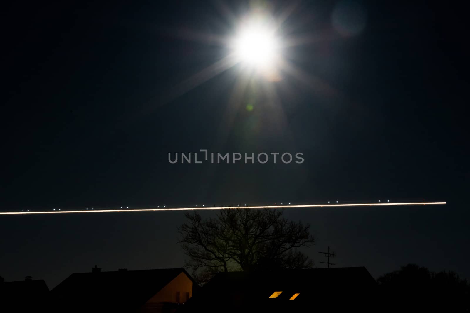 Bright moon shining over houses and trees with traces of a landing airplane