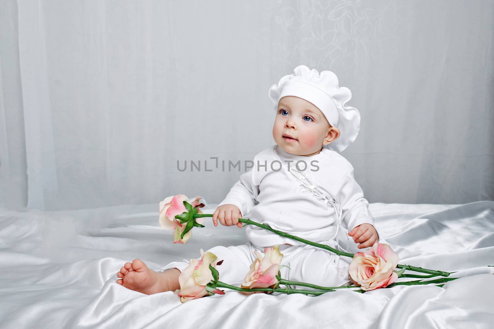 Little girl sitting on silk sheets lie at the feet of flowers