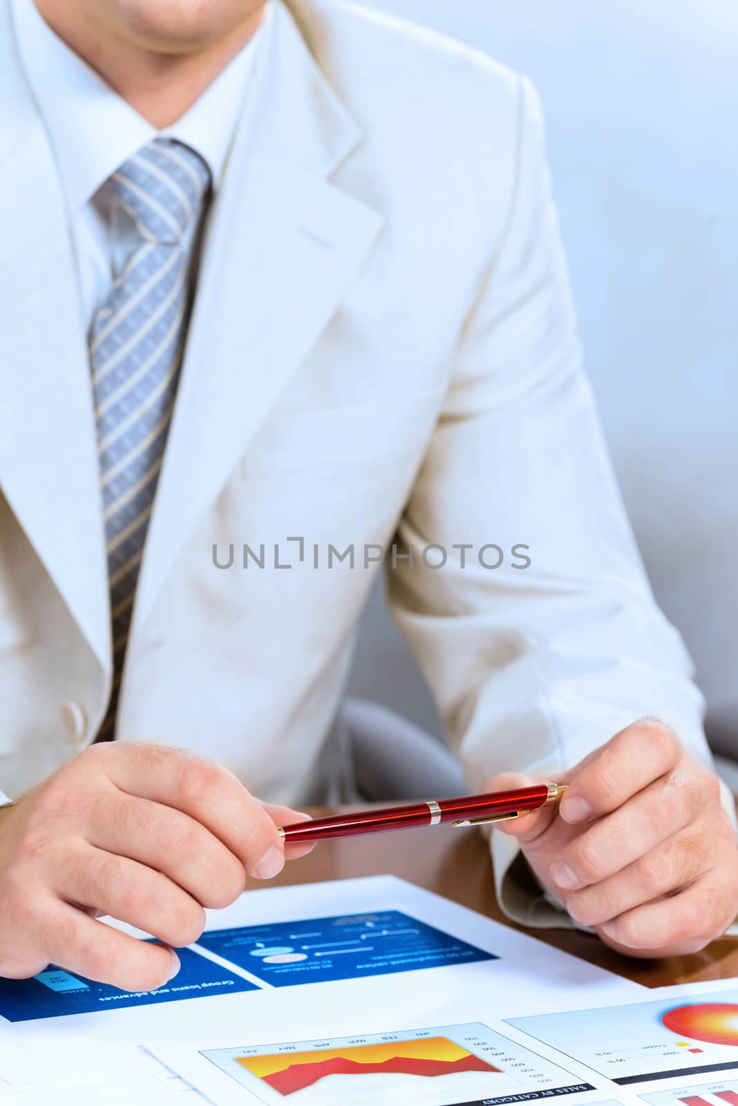businessman holding a pen in hand, in front of him laid paper business financial charts