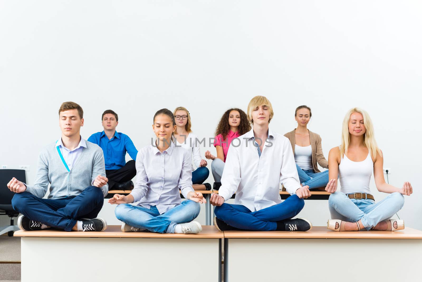 group of young people meditating in office at desk, group meditation