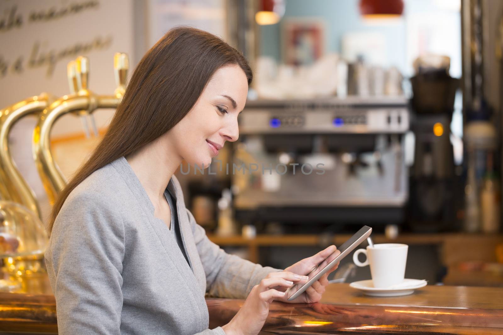 Beautiful young woman using her tablet pc in coffee bar  by LDProd