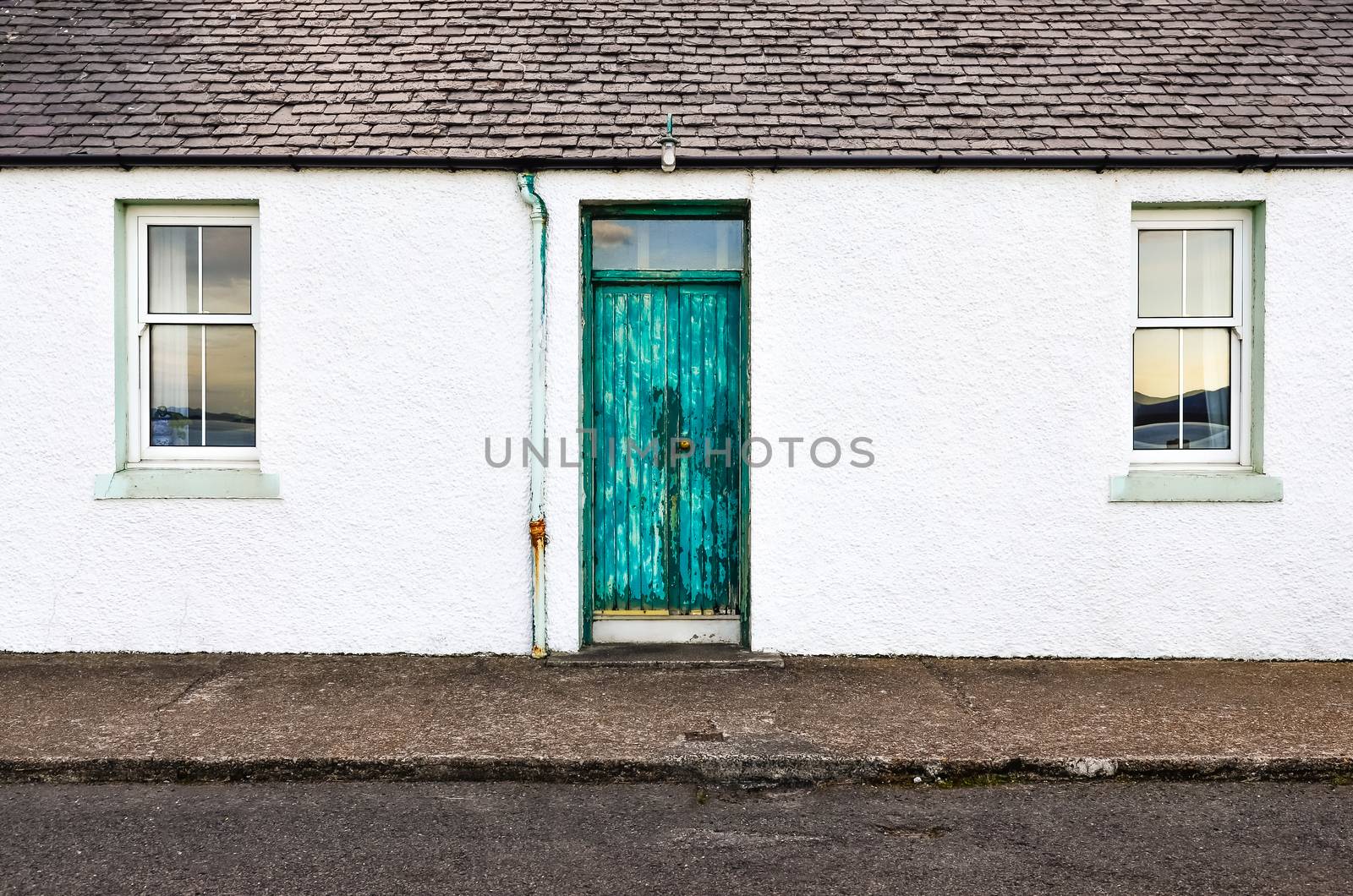 Detail of green door and two windows on white wall house