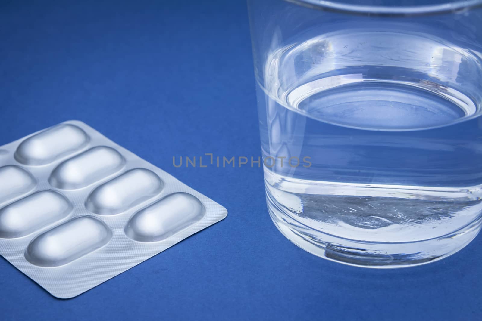 Glass of water and pills isolated on blue by digicomphoto
