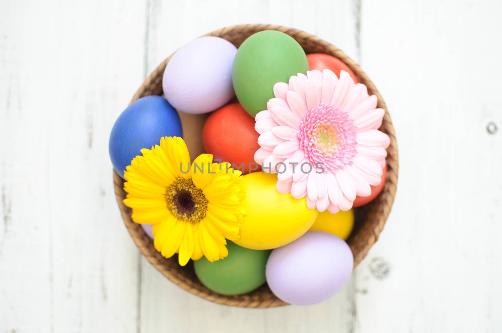 Easter eggs inside a wicker basket with daisies 