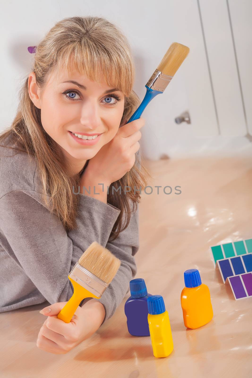 beautiful female painter lies on wooden floor and holding two paintbrushs and looking at camera