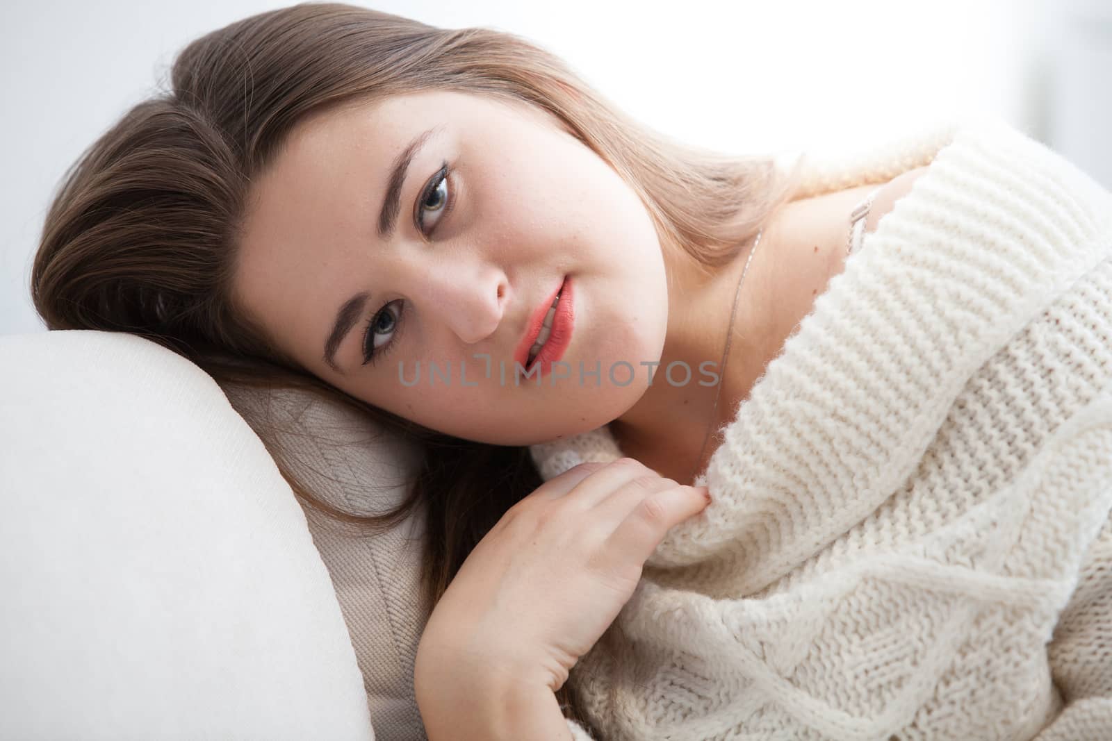 Sexy brunette woman in white woolen sweater sitting on sofa