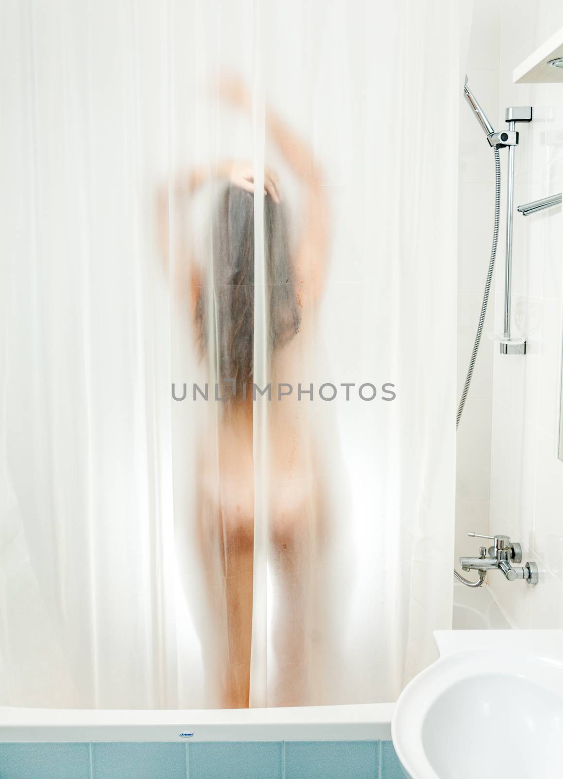Sexy woman standing in shower behind transparent curtain
