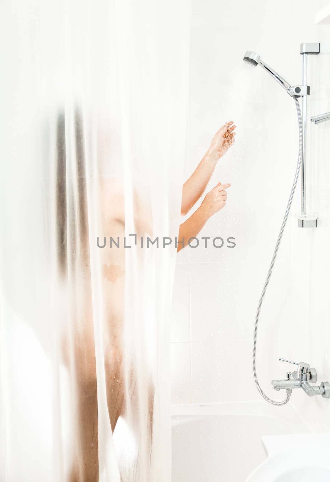 Brunette woman washing in shower behind transparent curtain