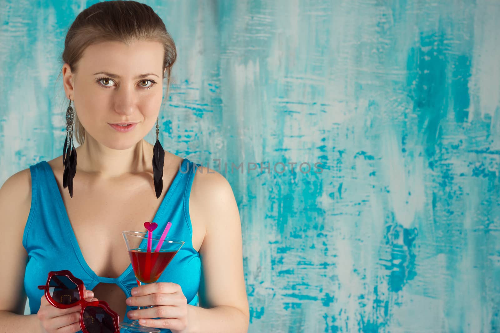 Happy beautiful woman holding a tropical cocktail with sunglasses on bright background