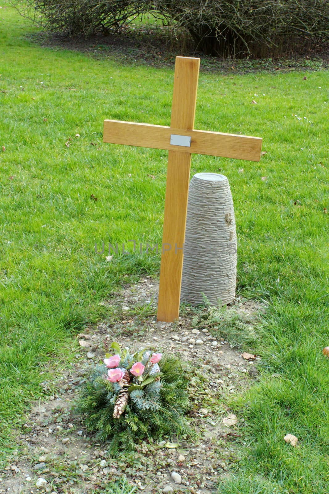 Simple wood cross and flower on a cemetery tomb in green grass