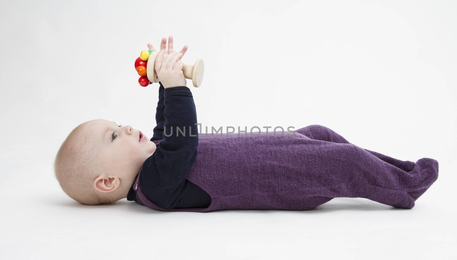 toddler lying on his back playing with wooden toy. grey background