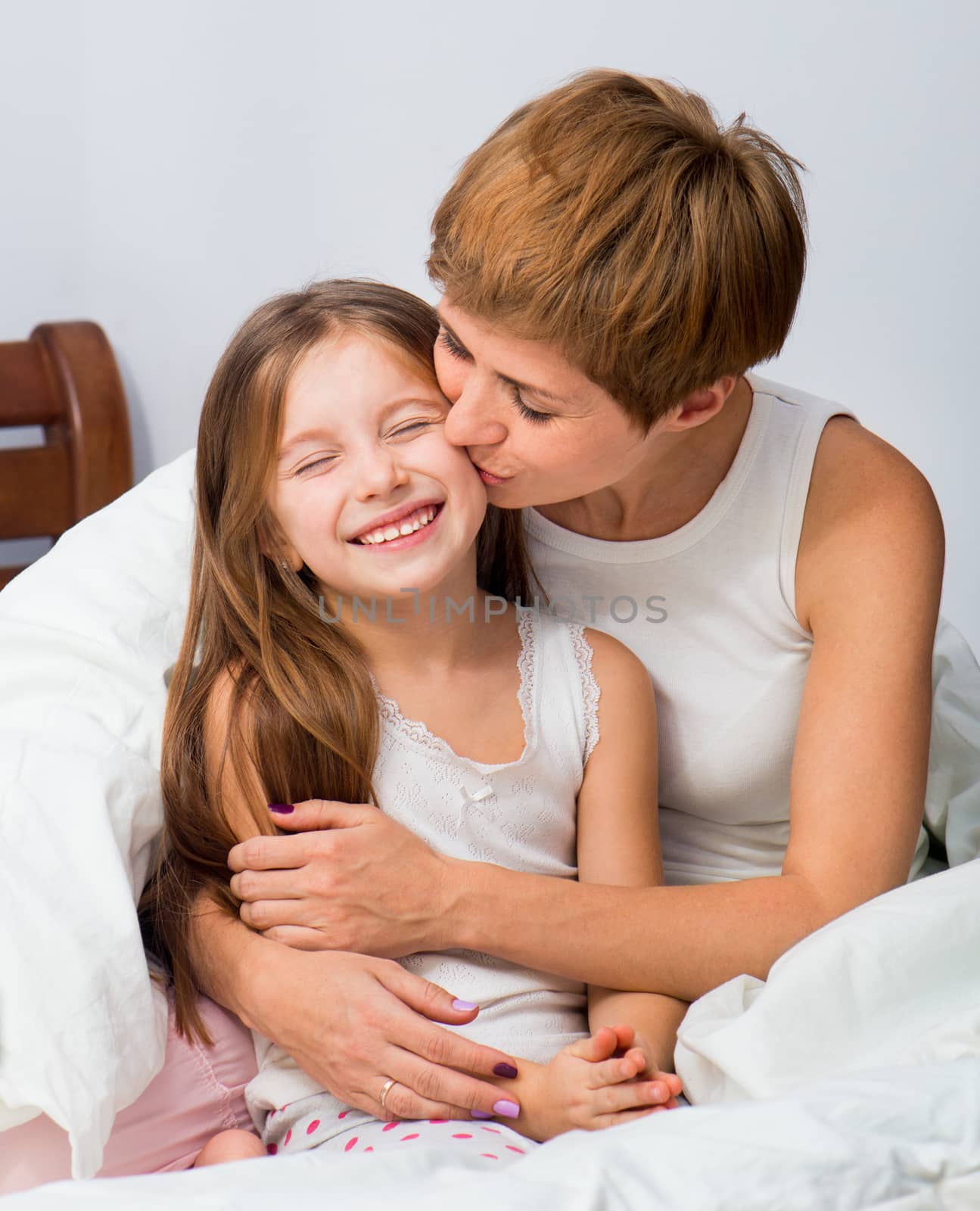 Mother kisses her daughter sitting on a bed