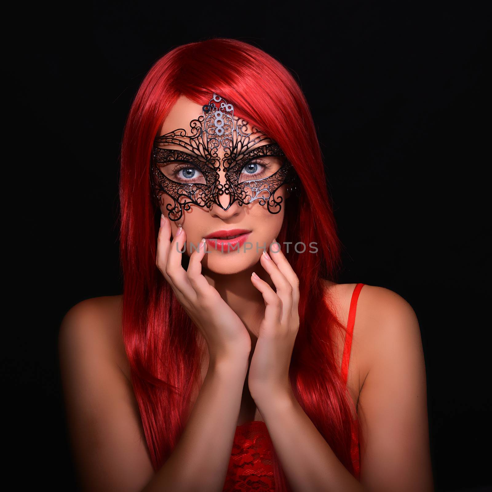 Beautiful red haired woman in carnival mask over black background