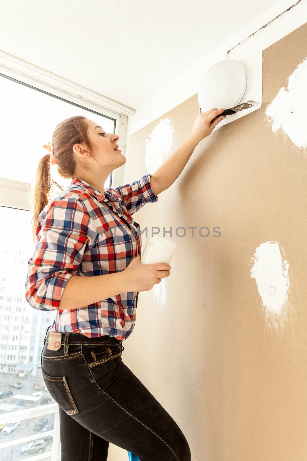 Female painter plastering gypsum cardboard wall